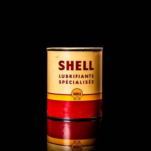 Vintage Shell oil can from 1950–1960 with white base color, yellow and red accents, and the classic Shell logo. Antique motor oil tin displayed in a studio setting against a solid black background.