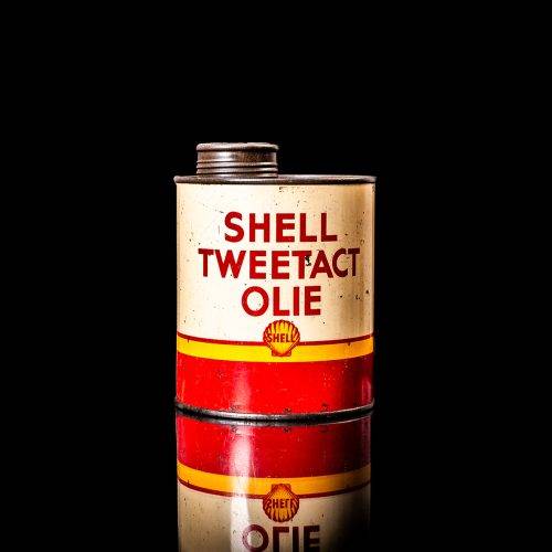 Vintage Shell oil can from 1950–1960 with white base color, yellow and red accents, and the classic Shell logo. Antique motor oil tin displayed in a studio setting against a solid black background.