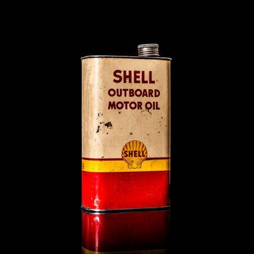 Vintage Shell oil can from 1950–1960 with white base color, yellow and red accents, and the classic Shell logo. Antique motor oil tin displayed in a studio setting against a solid black background.