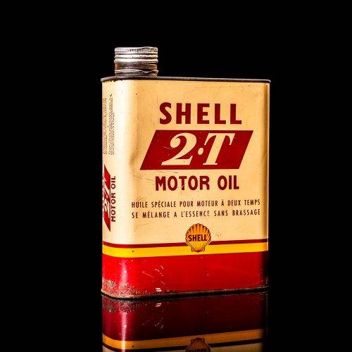 Vintage Shell oil can from 1950–1960 with white base color, yellow and red accents, and the classic Shell logo. Antique motor oil tin displayed in a studio setting against a solid black background.