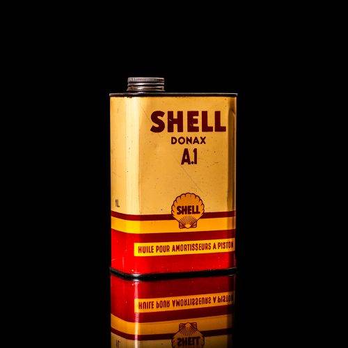 Vintage Shell oil can from 1950–1960 with white base color, yellow and red accents, and the classic Shell logo. Antique motor oil tin displayed in a studio setting against a solid black background.