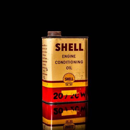 Vintage Shell oil can from 1950–1960 with white base color, yellow and red accents, and the classic Shell logo. Antique motor oil tin displayed in a studio setting against a solid black background.