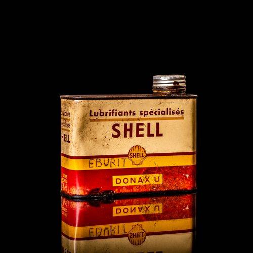 Vintage Shell oil can from 1950–1960 with white base color, yellow and red accents, and the classic Shell logo. Antique motor oil tin displayed in a studio setting against a solid black background.