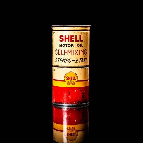 Vintage Shell oil can from 1950–1960 with white base color, yellow and red accents, and the classic Shell logo. Antique motor oil tin displayed in a studio setting against a solid black background."