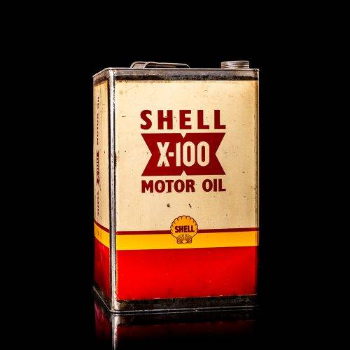 Vintage Shell oil can from 1950–1960 with white base color, yellow and red accents, and the classic Shell logo. Antique motor oil tin displayed in a studio setting against a solid black background."