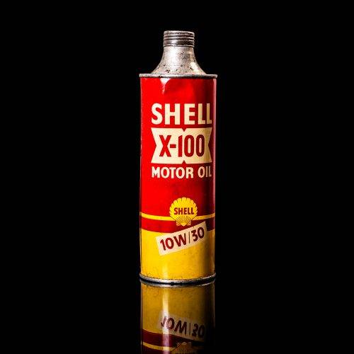 Vintage Shell oil can from 1950–1960 with white base color, yellow and red accents, and the classic Shell logo. Antique motor oil tin displayed in a studio setting against a solid black background."