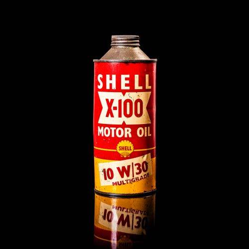 Vintage Shell oil can from 1950–1960 with white base color, yellow and red accents, and the classic Shell logo. Antique motor oil tin displayed in a studio setting against a solid black background."
