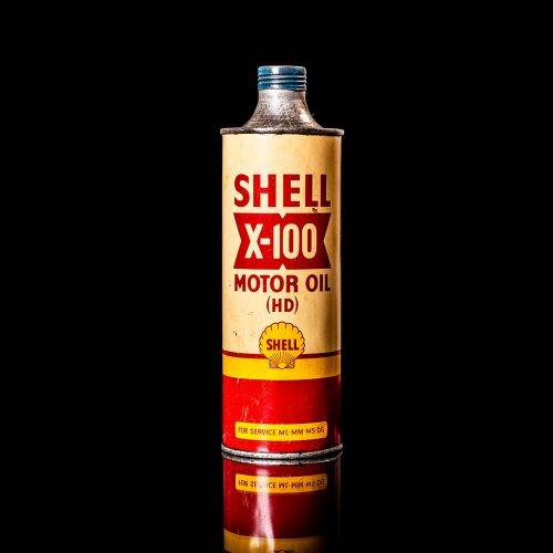 Vintage Shell oil can from 1950–1960 with white base color, yellow and red accents, and the classic Shell logo. Antique motor oil tin displayed in a studio setting against a solid black background."