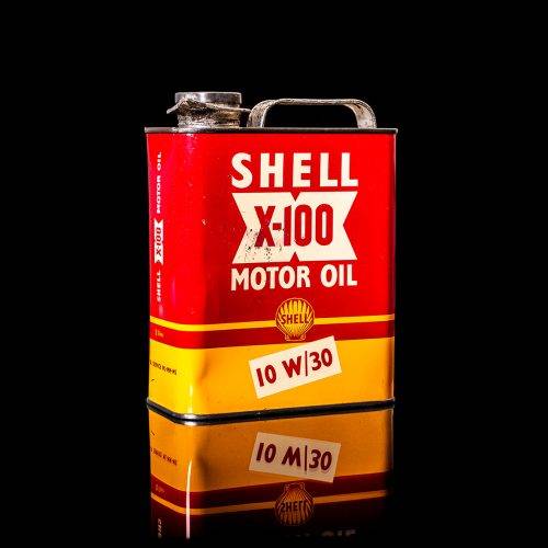 Vintage Shell oil can from 1950–1960 with white base color, yellow and red accents, and the classic Shell logo. Antique motor oil tin displayed in a studio setting against a solid black background."