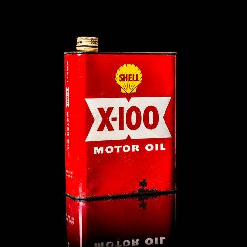 Vintage Shell oil can from 1950–1960 with white base color, yellow and red accents, and the classic Shell logo. Antique motor oil tin displayed in a studio setting against a solid black background."