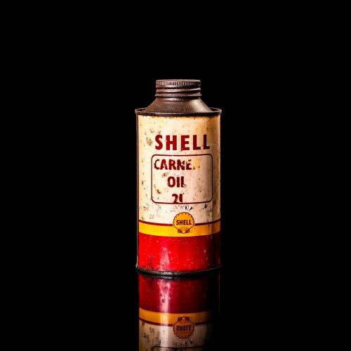 Vintage Shell oil can from 1950–1960 with white base color, yellow and red accents, and the classic Shell logo. Antique motor oil tin displayed in a studio setting against a solid black background."