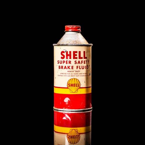 Vintage Shell oil can from 1950–1960 with white base color, yellow and red accents, and the classic Shell logo. Antique motor oil tin displayed in a studio setting against a solid black background."