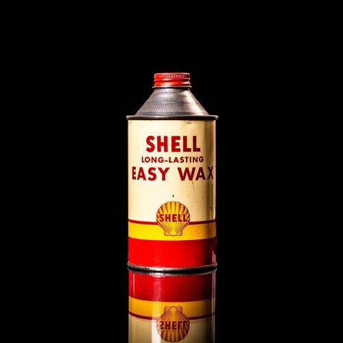 Vintage Shell oil can from 1950–1960 with white base color, yellow and red accents, and the classic Shell logo. Antique motor oil tin displayed in a studio setting against a solid black background."