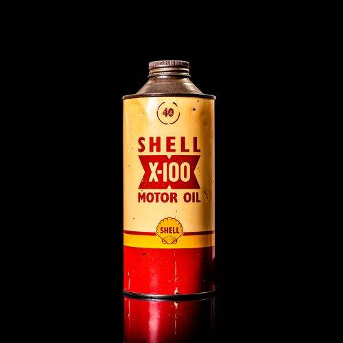 Vintage Shell oil can from 1950–1960 with white base color, yellow and red accents, and the classic Shell logo. Antique motor oil tin displayed in a studio setting against a solid black background."