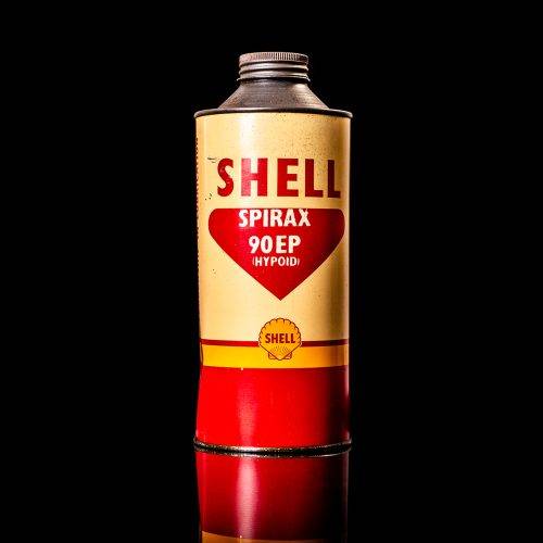 Vintage Shell oil can from 1950–1960 with white base color, yellow and red accents, and the classic Shell logo. Antique motor oil tin displayed in a studio setting against a solid black background."