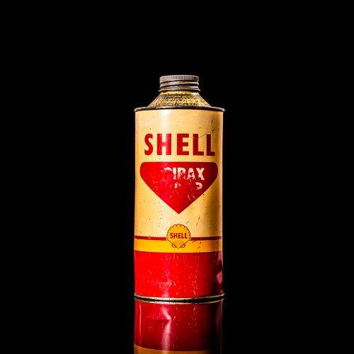 Vintage Shell oil can from 1950–1960 with white base color, yellow and red accents, and the classic Shell logo. Antique motor oil tin displayed in a studio setting against a solid black background."