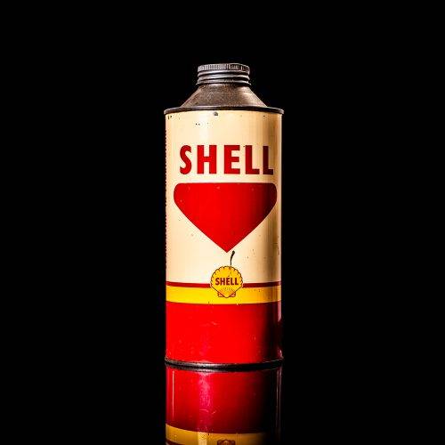 Vintage Shell oil can from 1950–1960 with white base color, yellow and red accents, and the classic Shell logo. Antique motor oil tin displayed in a studio setting against a solid black background."