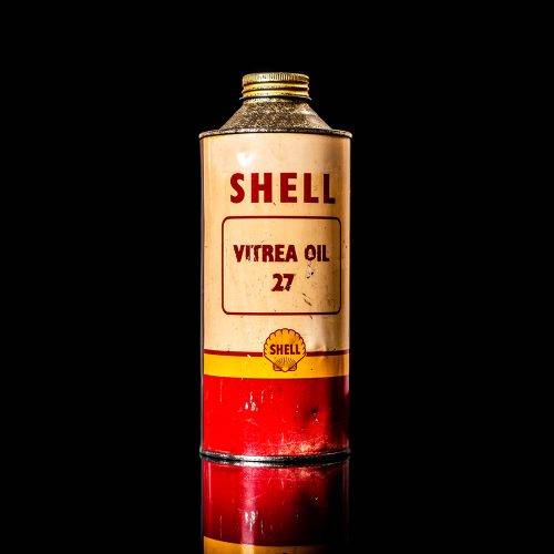 Vintage Shell oil can from 1950–1960 with white base color, yellow and red accents, and the classic Shell logo. Antique motor oil tin displayed in a studio setting against a solid black background."