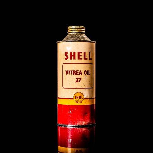 Vintage Shell oil can from 1950–1960 with white base color, yellow and red accents, and the classic Shell logo. Antique motor oil tin displayed in a studio setting against a solid black background."