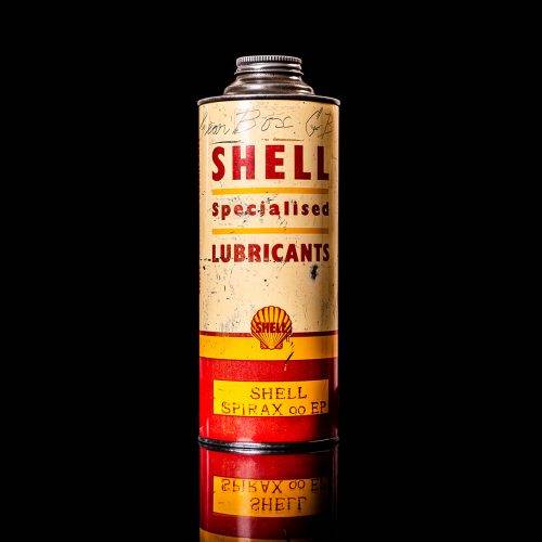 Vintage Shell oil can from 1950–1960 with white base color, yellow and red accents, and the classic Shell logo. Antique motor oil tin displayed in a studio setting against a solid black background."