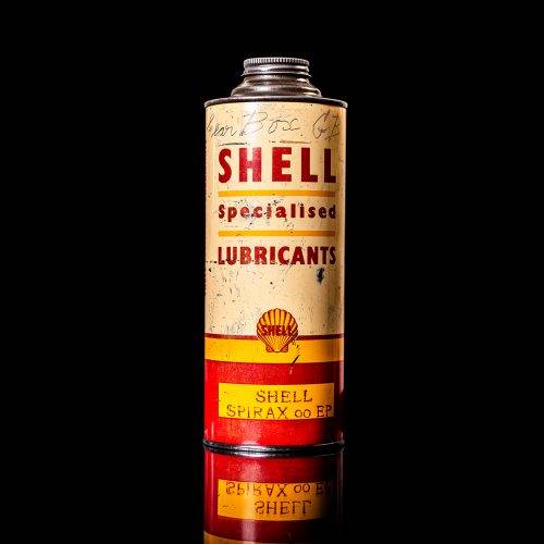Vintage Shell oil can from 1950–1960 with white base color, yellow and red accents, and the classic Shell logo. Antique motor oil tin displayed in a studio setting against a solid black background."