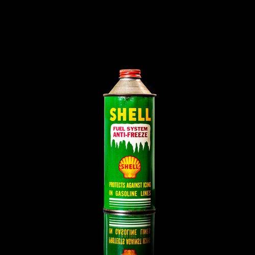 Vintage Shell oil can from 1950–1960 with white base color, yellow and red accents, and the classic Shell logo. Antique motor oil tin displayed in a studio setting against a solid black background."