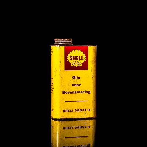 Vintage Shell oil can from 1950–1960 with white base color, yellow and red accents, and the classic Shell logo. Antique motor oil tin displayed in a studio setting against a solid black background."