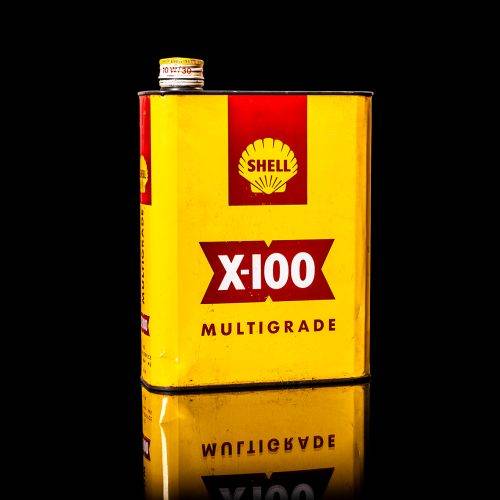 Vintage Shell oil can from 1950–1960 with white base color, yellow and red accents, and the classic Shell logo. Antique motor oil tin displayed in a studio setting against a solid black background."