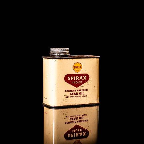 Vintage Shell oil can from 1950–1960 with white base color, yellow and red accents, and the classic Shell logo. Antique motor oil tin displayed in a studio setting against a solid black background."