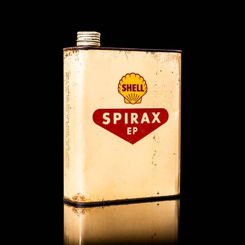 Vintage Shell oil can from 1950–1960 with white base color, yellow and red accents, and the classic Shell logo. Antique motor oil tin displayed in a studio setting against a solid black background."