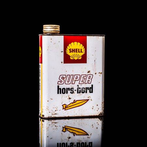 Vintage Shell oil can from 1950–1960 with white base color, yellow and red accents, and the classic Shell logo. Antique motor oil tin displayed in a studio setting against a solid black background."