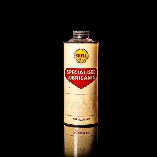 Vintage Shell oil can from 1950–1960 with white base color, yellow and red accents, and the classic Shell logo. Antique motor oil tin displayed in a studio setting against a solid black background."