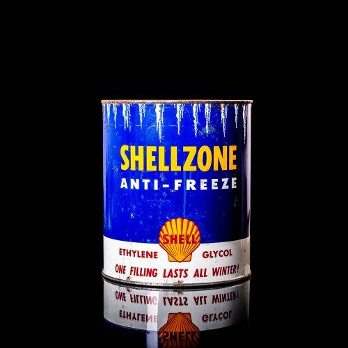 Vintage Shell oil can from 1950–1960 with white base color, yellow and red accents, and the classic Shell logo. Antique motor oil tin displayed in a studio setting against a solid black background."