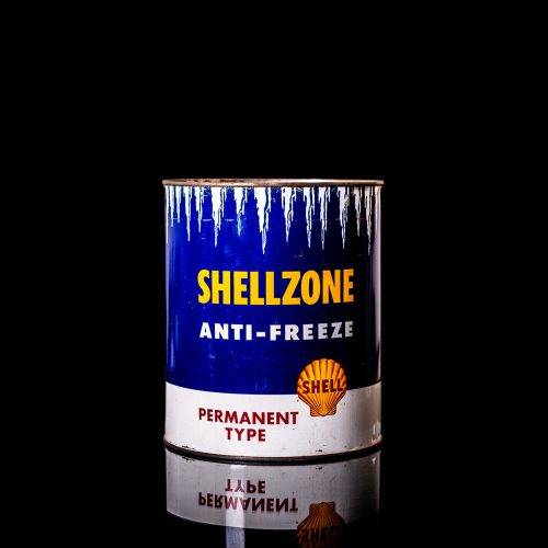 Vintage Shell oil can from 1950–1960 with white base color, yellow and red accents, and the classic Shell logo. Antique motor oil tin displayed in a studio setting against a solid black background."
