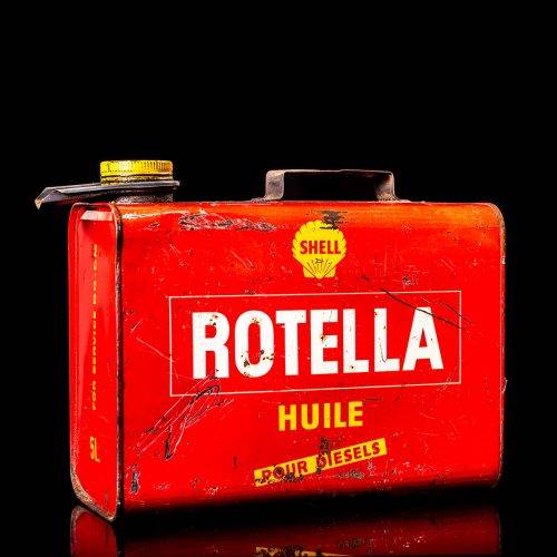 Vintage Shell oil can from 1950–1960 with white base color, yellow and red accents, and the classic Shell logo. Antique motor oil tin displayed in a studio setting against a solid black background."