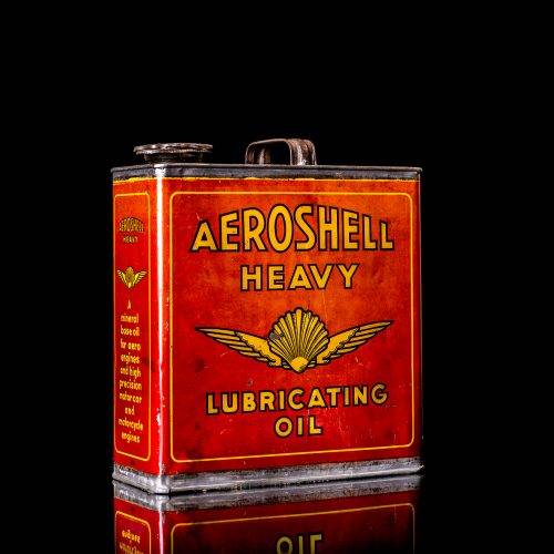 Rare and unique vintage Aeroshell oil can from 1900–1950 with red base and yellow accents, featuring the aeroShell logo. This antique motor oil tin is displayed in a studio setting against a solid black background.