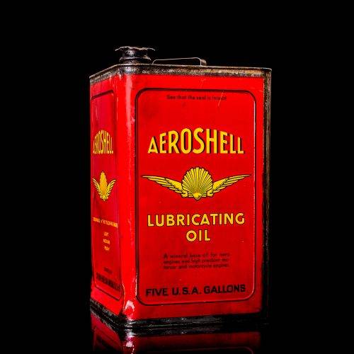 Rare and unique vintage Aeroshell oil can from 1900–1950 with red base and yellow accents, featuring the aeroShell logo. This antique motor oil tin is displayed in a studio setting against a solid black background.