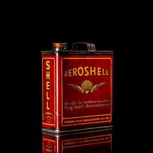 Rare and unique vintage Aeroshell oil can from 1900–1950 with red base and yellow accents, featuring the aeroShell logo. This antique motor oil tin is displayed in a studio setting against a solid black background.