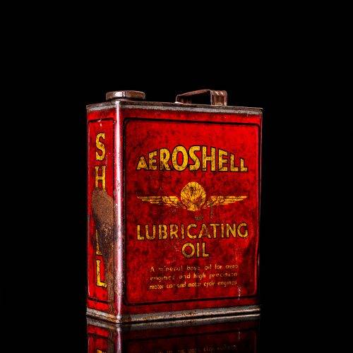 Rare and unique vintage Aeroshell oil can from 1900–1950 with red base and yellow accents, featuring the aeroShell logo. This antique motor oil tin is displayed in a studio setting against a solid black background.