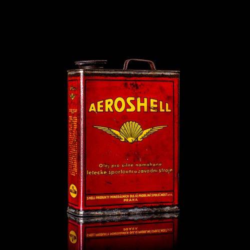 Rare and unique vintage Aeroshell oil can from 1900–1950 with red base and yellow accents, featuring the aeroShell logo. This antique motor oil tin is displayed in a studio setting against a solid black background.