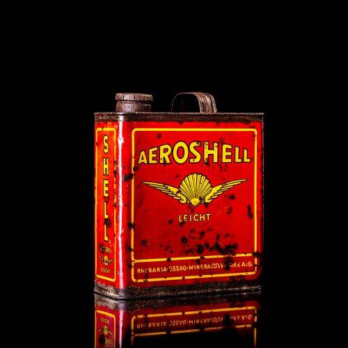 Rare and unique vintage Aeroshell oil can from 1900–1950 with red base and yellow accents, featuring the aeroShell logo. This antique motor oil tin is displayed in a studio setting against a solid black background.