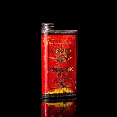 Rare and unique vintage Aeroshell oil can from 1900–1950 with red base and yellow accents, featuring the aeroShell logo. This antique motor oil tin is displayed in a studio setting against a solid black background.