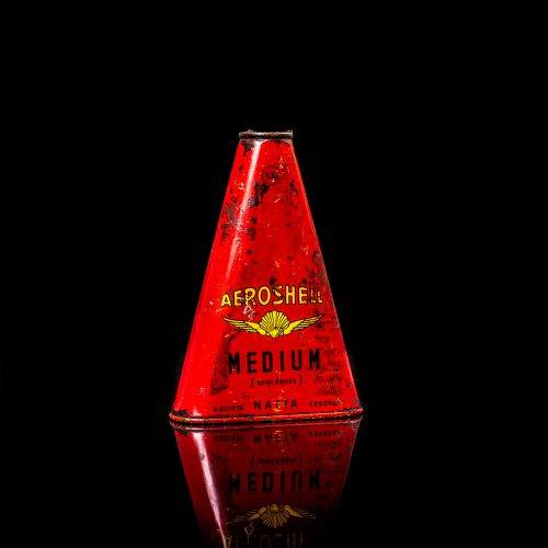 Rare and unique vintage Aeroshell oil can from 1900–1950 with red base and yellow accents, featuring the aeroShell logo. This antique motor oil tin is displayed in a studio setting against a solid black background.