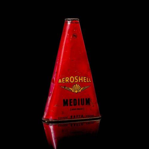 Rare and unique vintage Aeroshell oil can from 1900–1950 with red base and yellow accents, featuring the aeroShell logo. This antique motor oil tin is displayed in a studio setting against a solid black background.