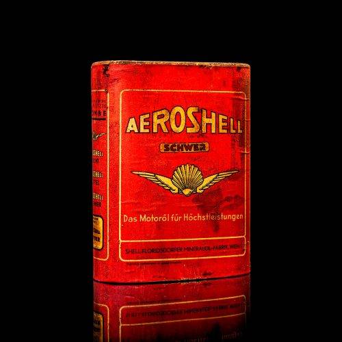 Rare and unique vintage Aeroshell oil can from 1900–1950 with red base and yellow accents, featuring the aeroShell logo. This antique motor oil tin is displayed in a studio setting against a solid black background.