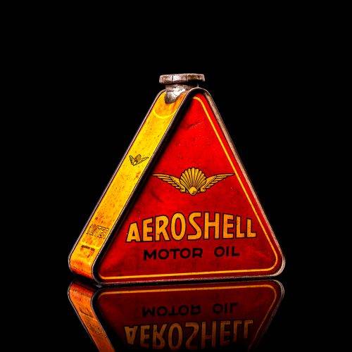 Rare and unique vintage Aeroshell oil can from 1900–1950 with red base and yellow accents, featuring the aeroShell logo. This antique motor oil tin is displayed in a studio setting against a solid black background.