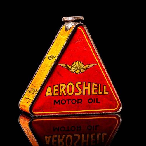 Rare and unique vintage Aeroshell oil can from 1900–1950 with red base and yellow accents, featuring the aeroShell logo. This antique motor oil tin is displayed in a studio setting against a solid black background.