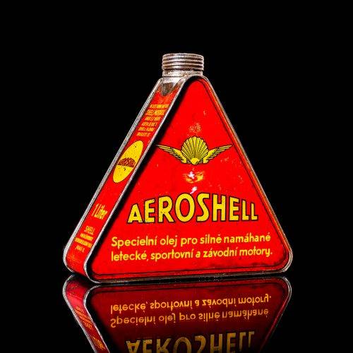 Rare and unique vintage Aeroshell oil can from 1900–1950 with red base and yellow accents, featuring the aeroShell logo. This antique motor oil tin is displayed in a studio setting against a solid black background.