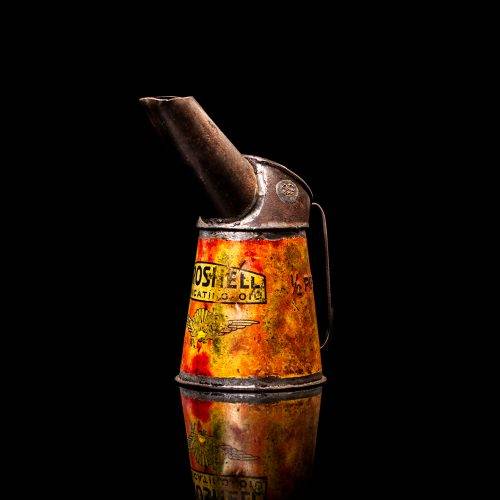 Rare and unique vintage Aeroshell oil can from 1900–1950 with red base and yellow accents, featuring the aeroShell logo. This antique motor oil tin is displayed in a studio setting against a solid black background.