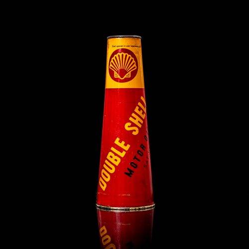 Rare and unique vintage conical shell oil can from 1900–1950 with a red base and yellow accents, featuring the classic shell logo. This antique, cone-shaped motor oil tin is showcased in a studio setting against a solid black background.